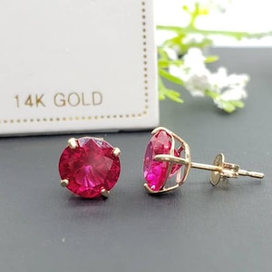 May include: A pair of 14k gold earrings with round, bright red ruby stones.