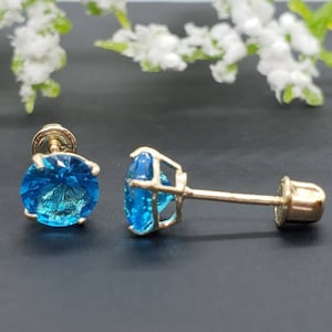 May include: A pair of gold stud earrings with blue topaz gemstones. The earrings have a simple design and are perfect for everyday wear.