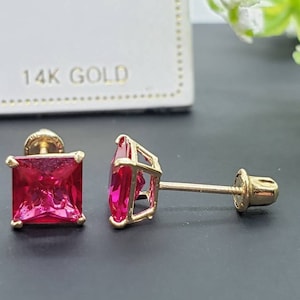 May include: A pair of 14k gold earrings with square-shaped red gemstones. The earrings have a screw-back closure.