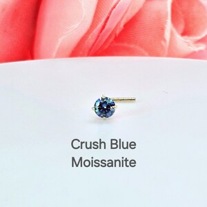 K&ouml;nnte beinhalten: Ein goldener Nasenring mit einem blauen Moissanit-Stein. Der Text "Crush Blue Moissanite" befindet sich unter dem Ring.