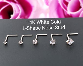 May include: Five 14K white gold L-shape nose studs arranged in a row, each featuring a clear round-cut gemstone of varying sizes set in a prong setting. The text 14K White Gold L-Shape Nose Stud is displayed above the jewelry pieces.