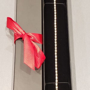 Puede incluir: Un brazalete de cadena de oro en una caja de regalo negra con una cinta roja.