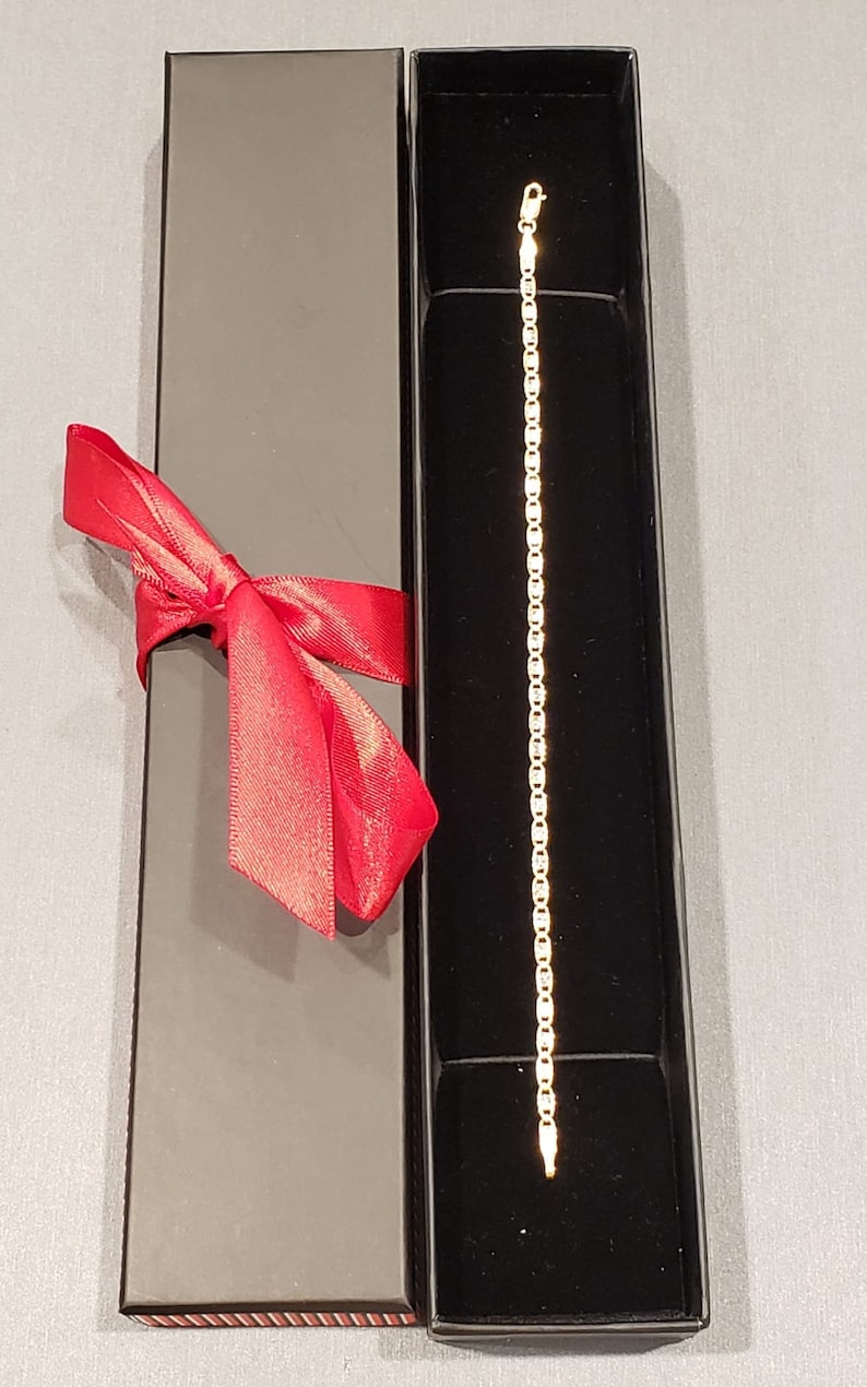 Puede incluir: Un brazalete de cadena de oro en una caja de regalo negra con una cinta roja.