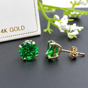 Könnte beinhalten: Ein Paar Ohrstecker aus 14-karätigem Gold mit runden, leuchtend grünen Edelsteinen. Ein Ohrring ist von vorne zu sehen, der andere von der Seite, wobei die Goldfassung und der Stift sichtbar sind. Der Text 14K GOLD ist zu sehen.