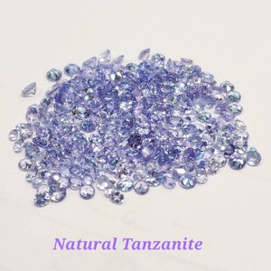 May include: A pile of loose natural Tanzanite gemstones. The stones are a light purple color and have a slight shimmer.