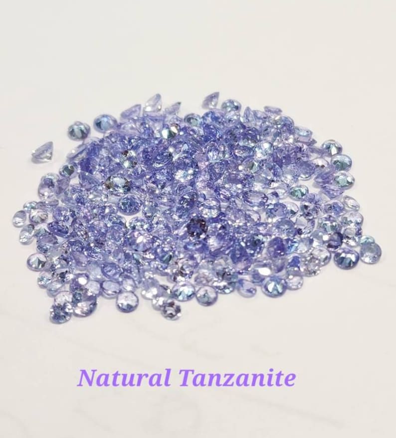 May include: A pile of loose natural Tanzanite gemstones. The stones are a light purple color and have a slight shimmer.