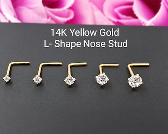 May include: Five 14K yellow gold L-shape nose studs arranged in a row, each featuring a single clear round prong-set gemstone that increases in size from left to right. The text 14K Yellow Gold L- Shape Nose Stud is centered above the jewelry.