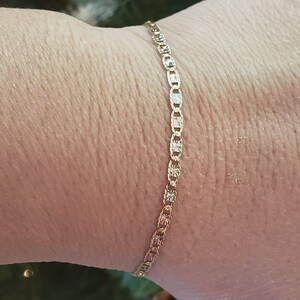 Puede incluir: Un brazalete de cadena de oro con un dise&ntilde;o delicado y estampado. La cadena est&aacute; hecha de peque&ntilde;os eslabones ovalados con un patr&oacute;n de diamante.