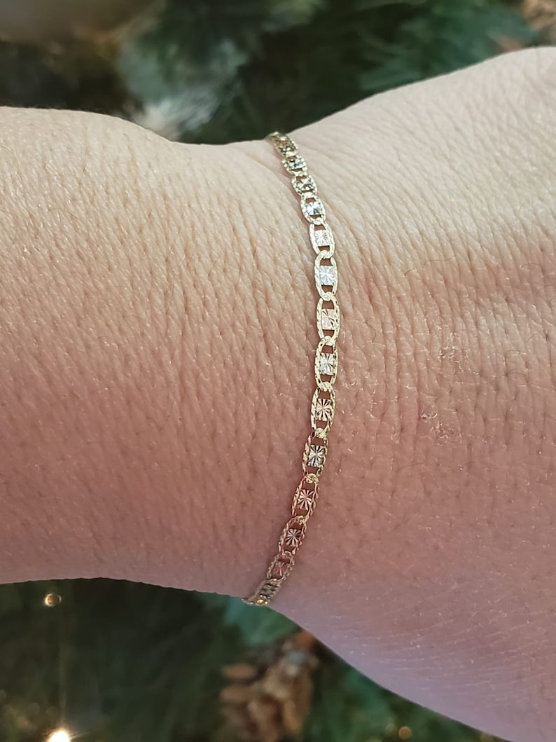 Puede incluir: Un brazalete de cadena de oro con un dise&ntilde;o delicado y estampado. La cadena est&aacute; hecha de peque&ntilde;os eslabones ovalados con un patr&oacute;n de diamante.