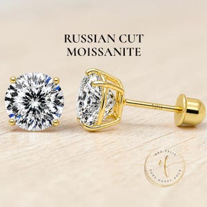 May include: A pair of gold stud earrings featuring Russian cut moissanite stones. The earrings have a round, brilliant-cut design with a gold setting and post. The text "Russian Cut Moissanite" is displayed above the earrings.