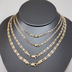 May include: Four gold chains of different lengths, all with a mariner link pattern. The chains are layered on a black velvet background.