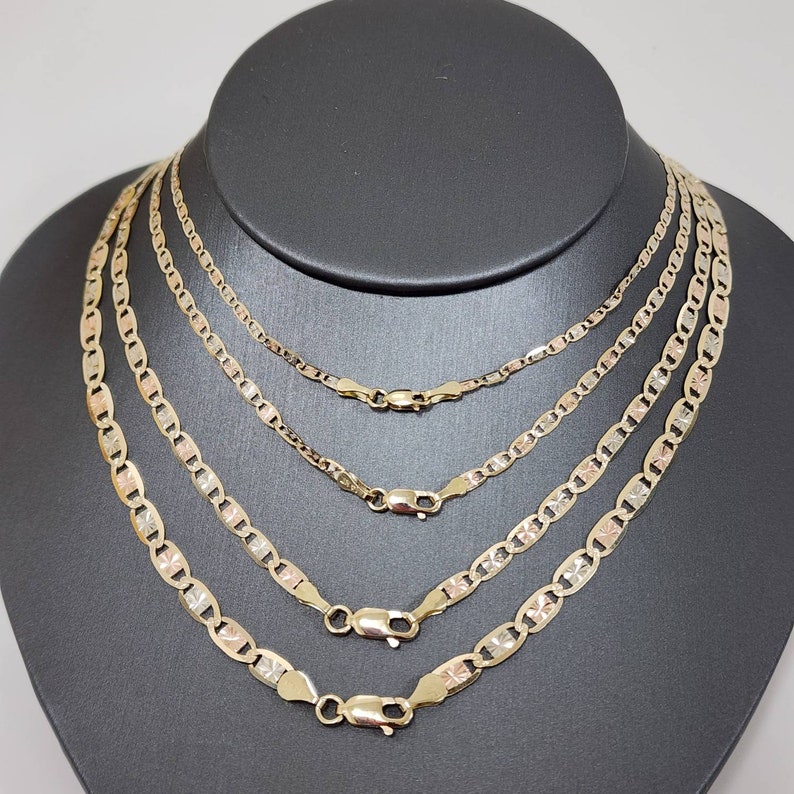 May include: Four gold chains of different lengths, all with a mariner link pattern. The chains are layered on a black velvet background.
