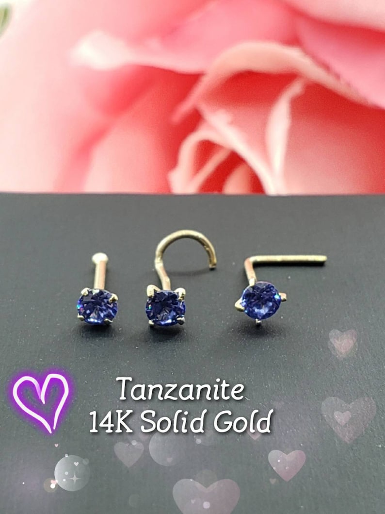 May include: Three 14K solid gold nose rings with a blue Tanzanite gemstone. The rings are on a black background.