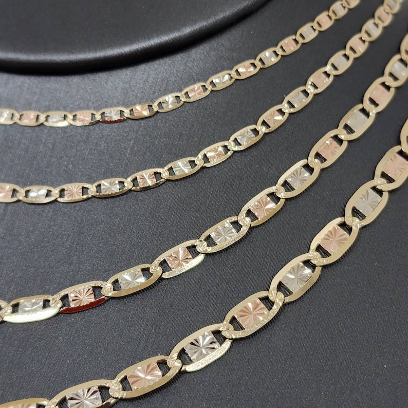 May include: Five gold chains with a diamond-shaped pattern on each link. The chains are layered on top of each other and are made of different shades of gold, including yellow, white, and rose gold.
