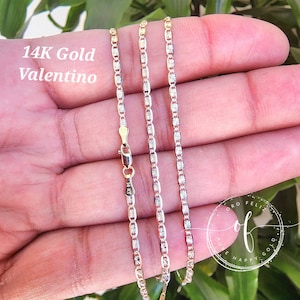 May include: A 14K gold Valentino chain necklace with a delicate, patterned design. The chain is shown on a hand, with the clasp visible.