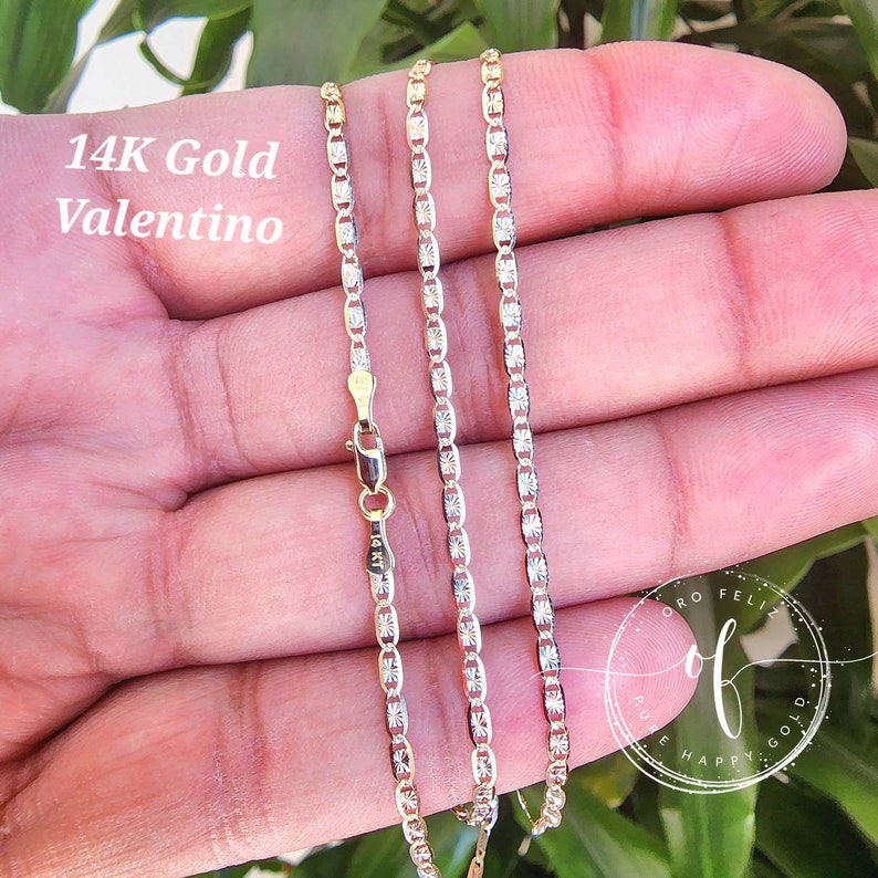 May include: A 14K gold Valentino chain necklace with a delicate, patterned design. The chain is shown on a hand, with the clasp visible.
