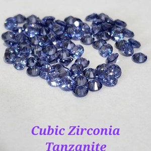 May include: A close-up of a pile of loose cubic zirconia gemstones in a vibrant blue-purple color, resembling tanzanite.