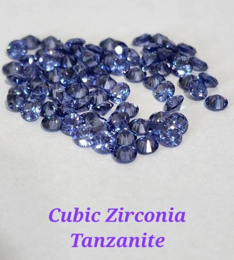 May include: A close-up of a pile of loose cubic zirconia gemstones in a vibrant blue-purple color, resembling tanzanite.