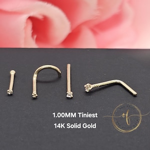 Puede incluir: Cuatro anillos de nariz de oro, cada uno con un pequeño diamante. Los anillos son de 1,00 mm y están hechos de oro sólido de 14 quilates. El texto "1,00 MM Tiniest 14K Solid Gold" es visible debajo de los anillos.