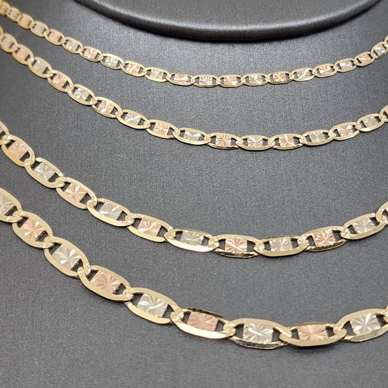 May include: Four gold chains of different lengths, each with a mariner link design. The chains are made of three-tone gold, with yellow, white, and rose gold links.