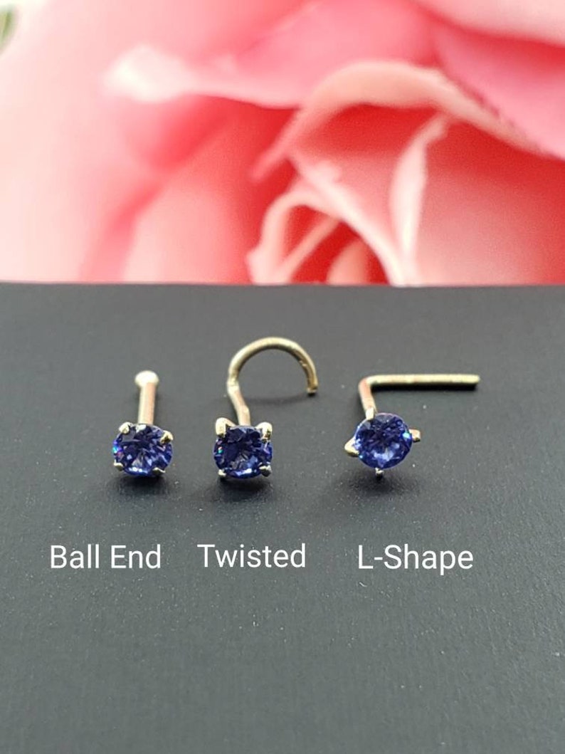 May include: Three nose rings with a blue gemstone. The rings are shown on a black surface. The rings are labeled "Ball End", "Twisted", and "L-Shape".