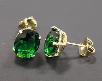 May include: A pair of gold earrings with oval-shaped green gemstones. The earrings have a post and butterfly back.