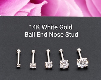 Könnte beinhalten: Fünf Nasenstecker aus 14-karätigem Weißgold mit Kugelende und klaren, rund geschliffenen Edelsteinen in verschiedenen Größen, in einer Reihe angeordnet. Der Text 14K White Gold Ball End Nose Stud steht auf dunklem Grund.