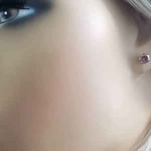 Peut inclure: Gros plan sur une oreille avec une petite boucle d'oreille ronde en pierre pr&eacute;cieuse violette.