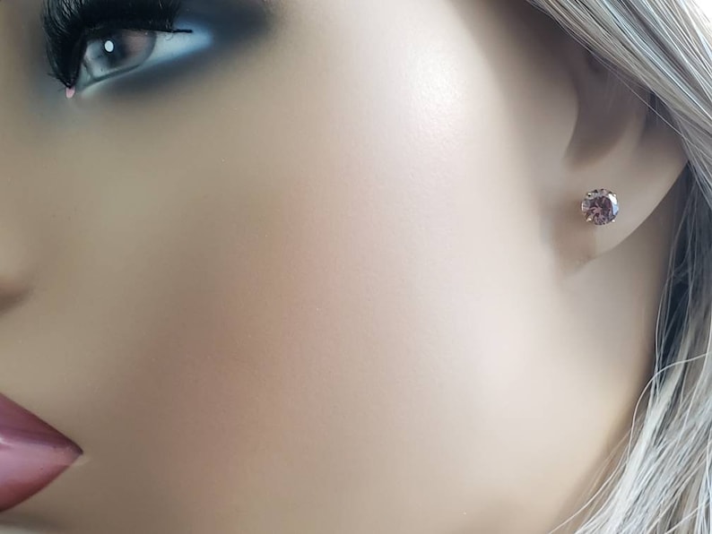 Peut inclure: Gros plan sur une oreille avec une petite boucle d'oreille ronde en pierre pr&eacute;cieuse violette.