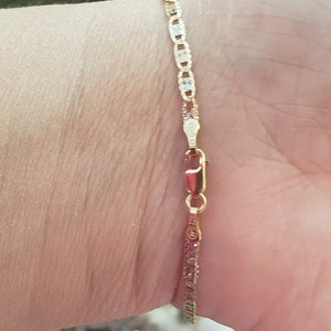 Puede incluir: Un brazalete de cadena de oro con un dise&ntilde;o de eslab&oacute;n marinero. El brazalete est&aacute; en la mu&ntilde;eca de una persona.