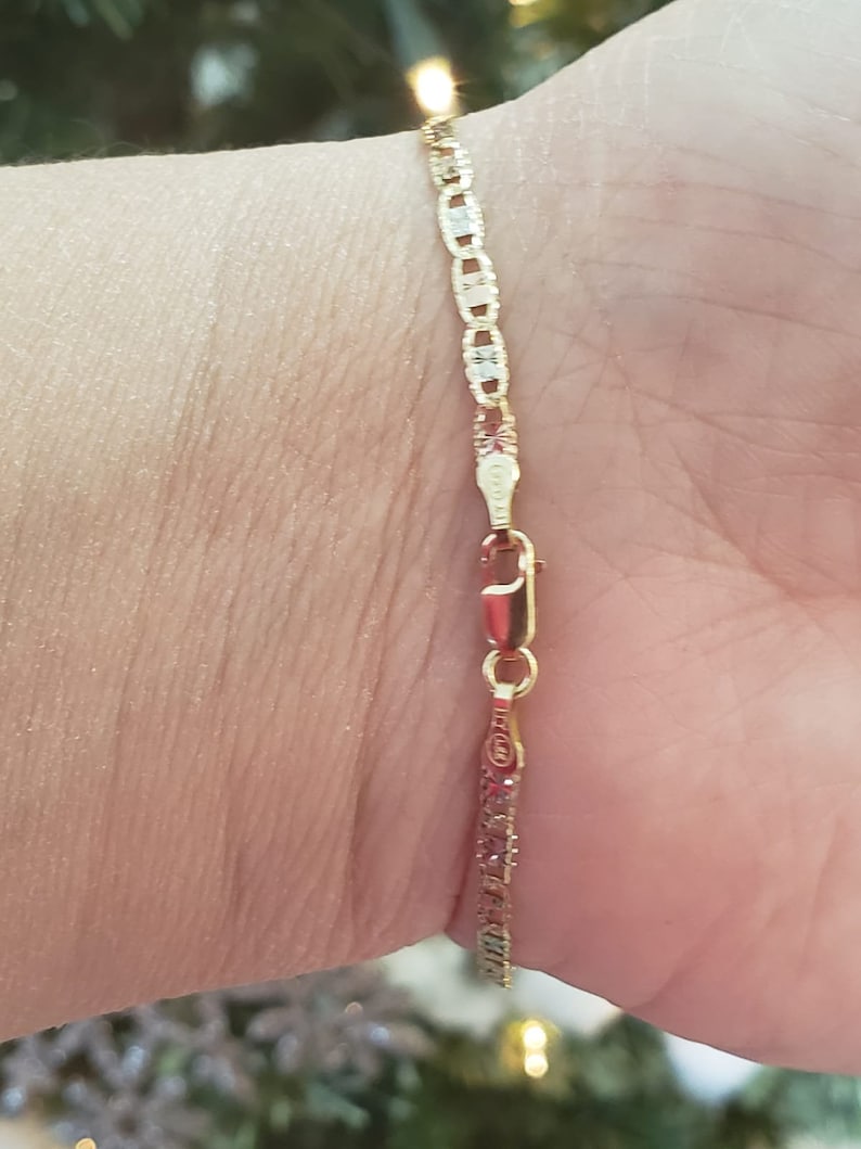 Puede incluir: Un brazalete de cadena de oro con un dise&ntilde;o de eslab&oacute;n marinero. El brazalete est&aacute; en la mu&ntilde;eca de una persona.