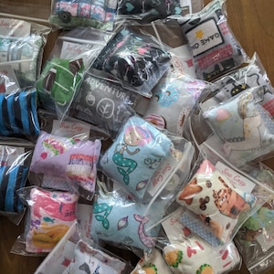 Könnte beinhalten: Eine Auswahl an bunten Katzenminzspielzeugen in verschiedenen Mustern und Designs, darunter eine Meerjungfrau, ein Einhorn, ein Taco und eine Katze. Die Spielzeuge sind in durchsichtigen Plastiktüten verpackt, auf denen der Markenname "Sew Cozy" steht.