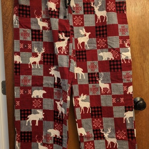 Puede incluir: Pantalones de pijama de cuadros rojos y grises con un patrón de renos y alces blancos.