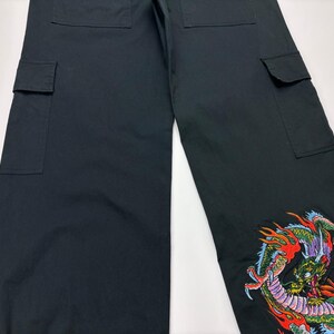 May include: Black cargo pants with multiple pockets and a colorful embroidered dragon design on the lower leg. The dragon features red, green, and yellow accents.