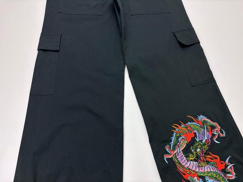 May include: Black cargo pants with multiple pockets and a colorful embroidered dragon design on the lower leg. The dragon features red, green, and yellow accents.