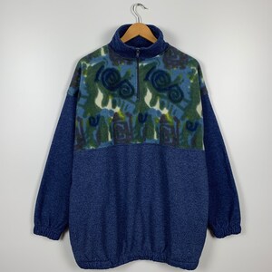 May include: A blue fleece pullover with a half-zip closure. The top half of the sweater features a colorful abstract pattern in shades of blue, green, and white.