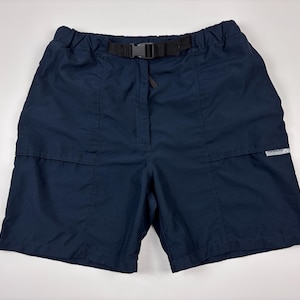 May include: Navy blue shorts with a black belt and buckle. The shorts have a drawstring waist and two front pockets. A small white tag is visible on the side. These shorts are suitable for outdoor activities.