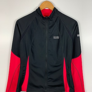 Könnte beinhalten: Schwarze und rote Laufjacke mit Reißverschluss und dem Logo "GORE RUNNING WEAR" auf der Vorderseite.