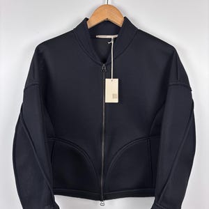 May include: A black zip-up jacket made from a mesh fabric with a tag hanging from the zipper.