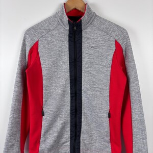 May include: A gray and red zip-up jacket with a black zipper and a small logo on the right side.