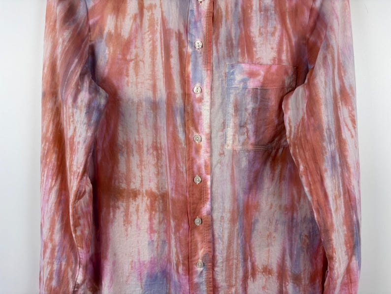 Pode incluir: Camisa de bot&atilde;o de manga comprida com um padr&atilde;o semelhante a aquarela em tons de rosa, roxo e castanho. A camisa tem um bolso no peito e o tecido parece leve e semi-transparente.