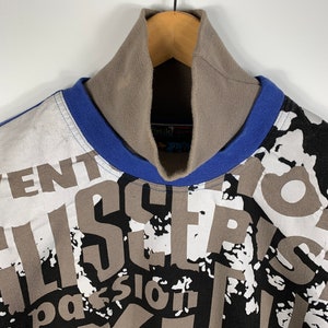 Puede incluir: Un jersey de cuello alto con estampado blanco, azul y negro con las palabras "Aventur", "Alisier", "Passion" y "Vor" impresas en la parte delantera.