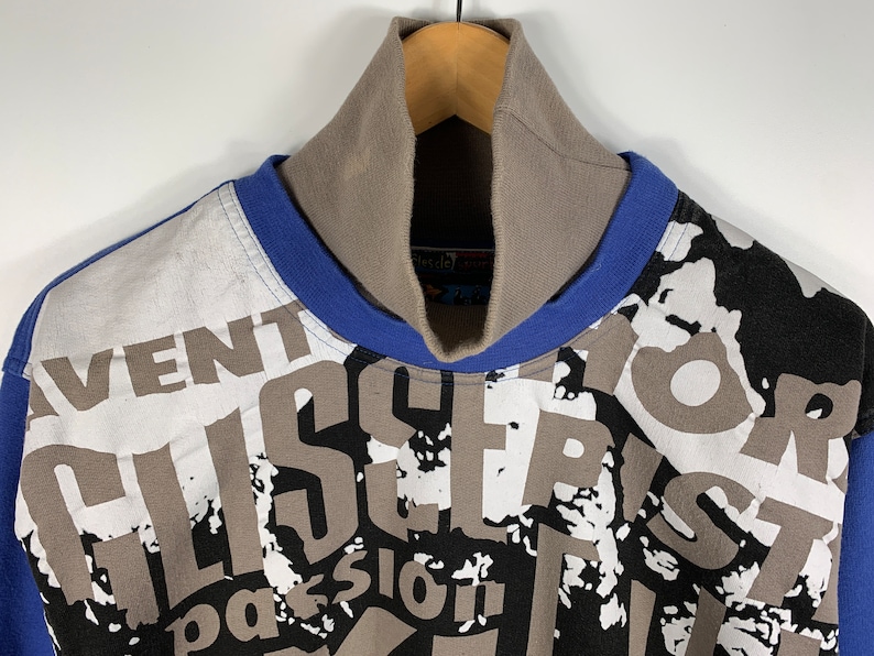 Puede incluir: Un jersey de cuello alto con estampado blanco, azul y negro con las palabras "Aventur", "Alisier", "Passion" y "Vor" impresas en la parte delantera.