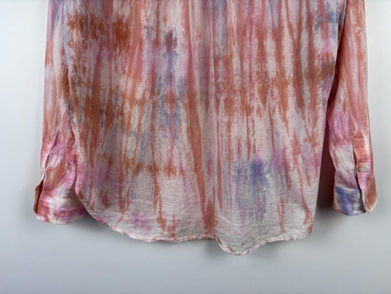Pode incluir: Uma camisa de manga comprida com um padr&atilde;o tie-dye em tons de rosa, laranja e roxo. A camisa tem uma frente abotoada e punhos. O tecido parece leve e fluido, com um brilho subtil.