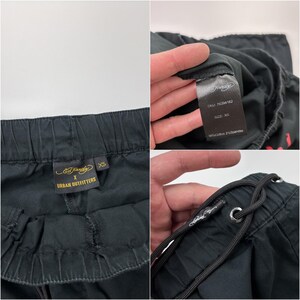 May include: Black drawstring pants with an elastic waistband. The pants have a tag that says "Ed Hardy X Urban Outfitters" and another tag with the size "XS". The pants are made of 98% cotton and 2% spandex.