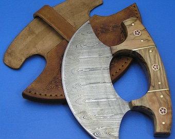 Op de afbeelding: Een gebogen, zilverkleurig mes met een houten handvat. Het handvat heeft een decoratief ontwerp met rode en gouden accenten. Het mes zit in een bruine leren schede.