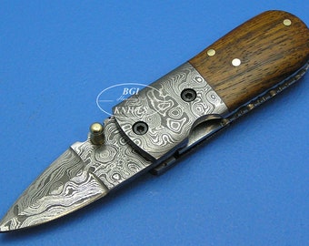 May include: A small, folding pocket knife with a wood handle and a patterned steel blade. The blade is partially open, revealing a detailed, swirling pattern.