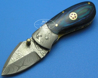 May include: A small, folding pocket knife with a Damascus steel blade and a blue and black patterned handle. The handle has a gold inlay with a red center.