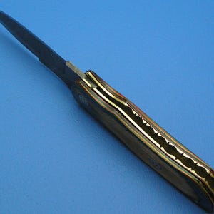 May include: A handcrafted folding knife with a dark blade and a handle featuring a multi-colored wood grain design. The handle is accented with brass and a decorative pattern.