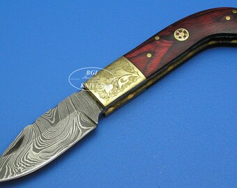 May include: A folding pocket knife with a red wood handle and a patterned steel blade. The handle has gold accents and an engraved design.